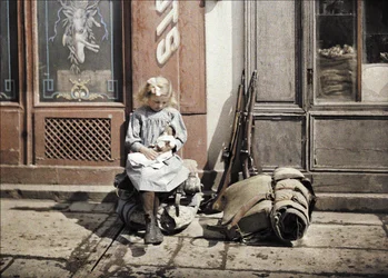 Kislány játszik a babájával, mellette a földön két pisztoly és egy hátizsák, Reims, Marne, Franciaország, 1917 (autokróm)